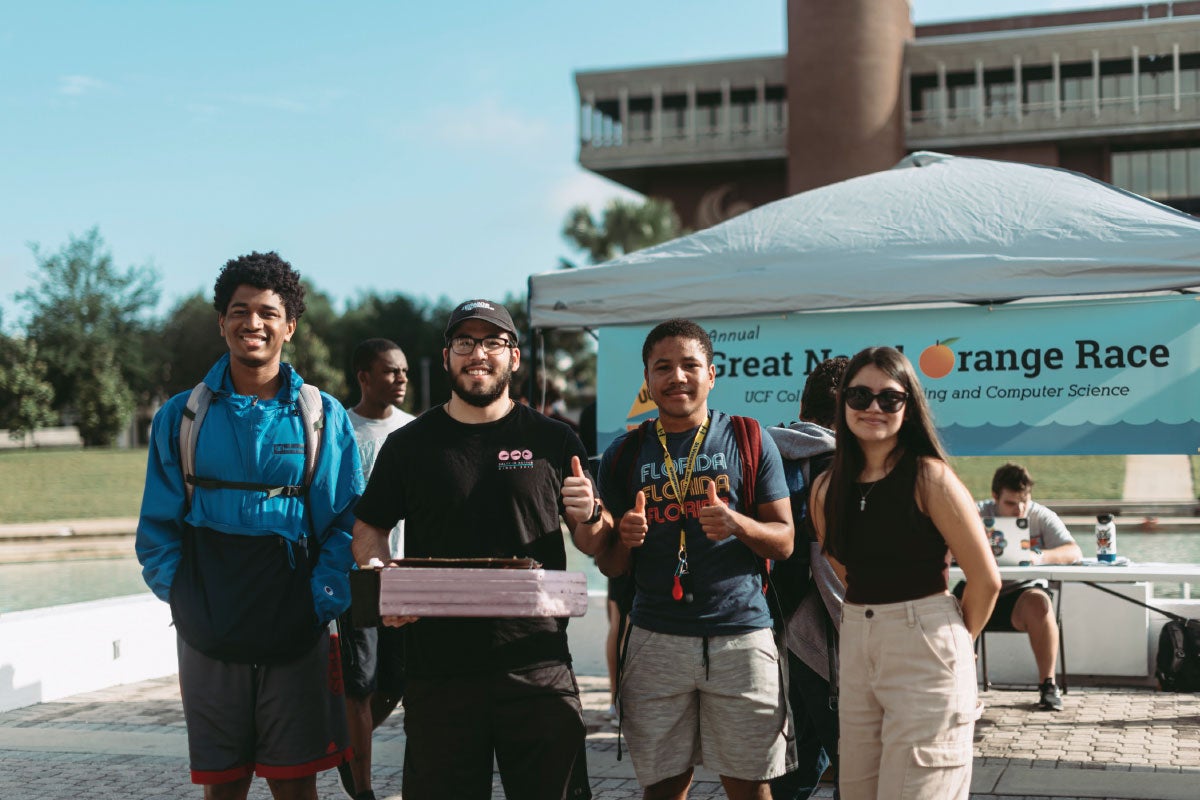 Four students with their watercraft in front of the UCF reflecting pond.