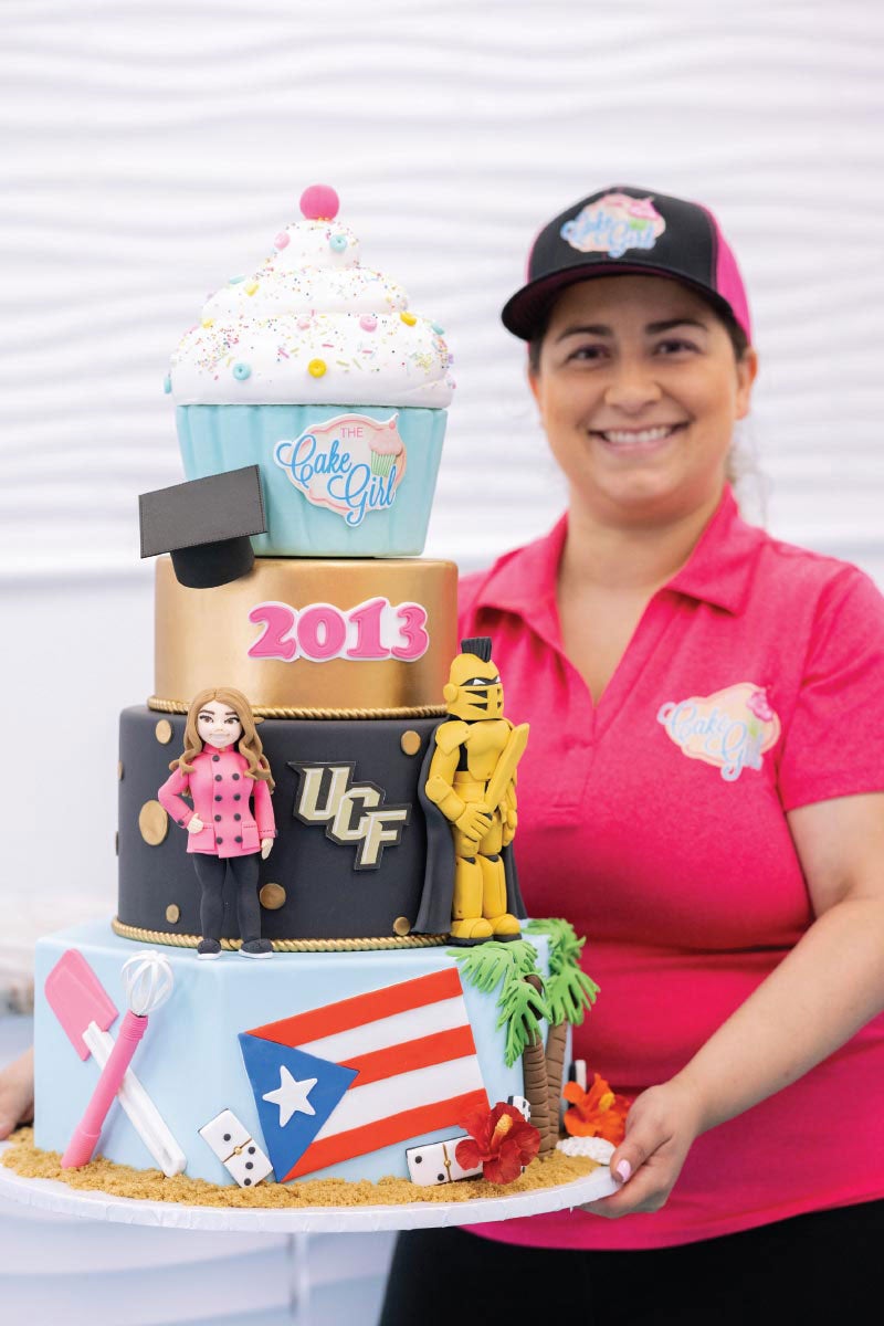 Kristina Lavellee holds a four layer cake that includes elements that represent Puerto Rico, baking, UCF, herself and her bakery.