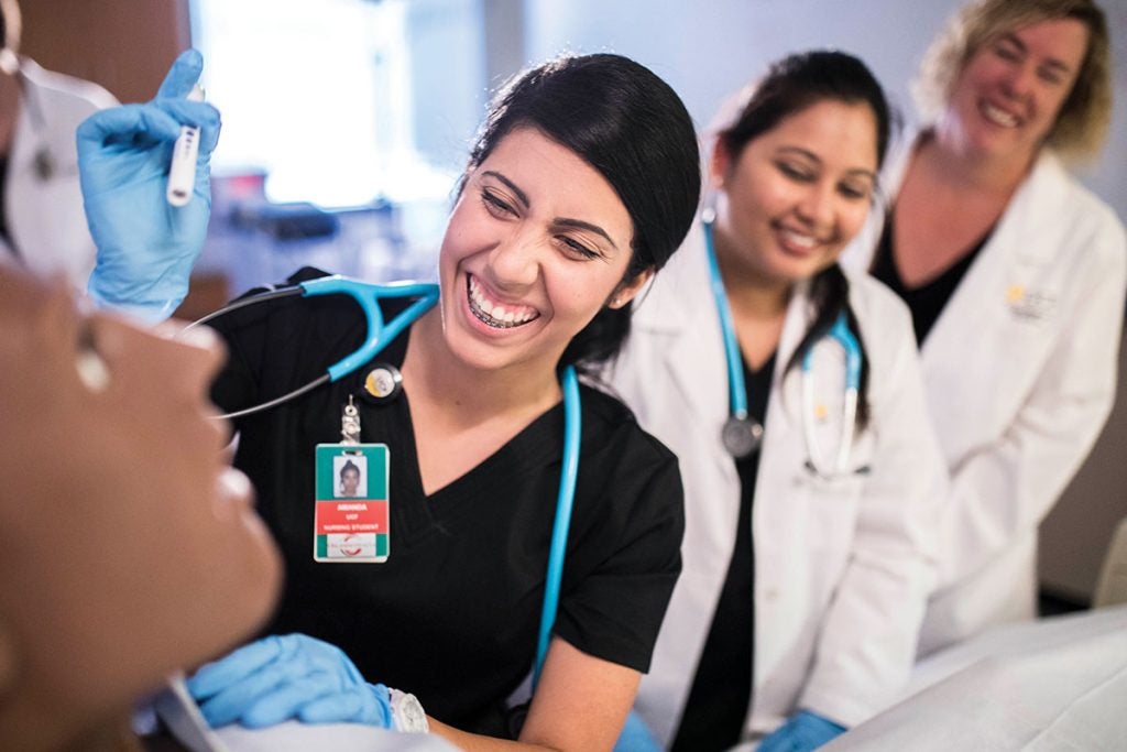 A UCF College of Nursing student works with a manikin while faculty oversee her.