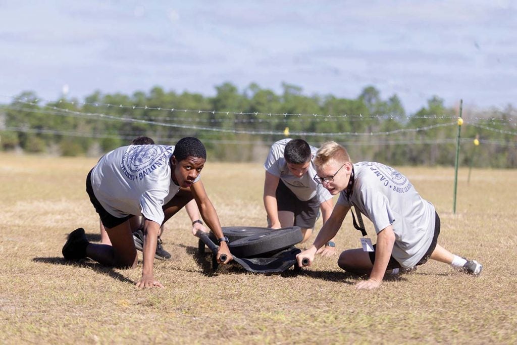 A team of four crawls and pull weights under barbed wire