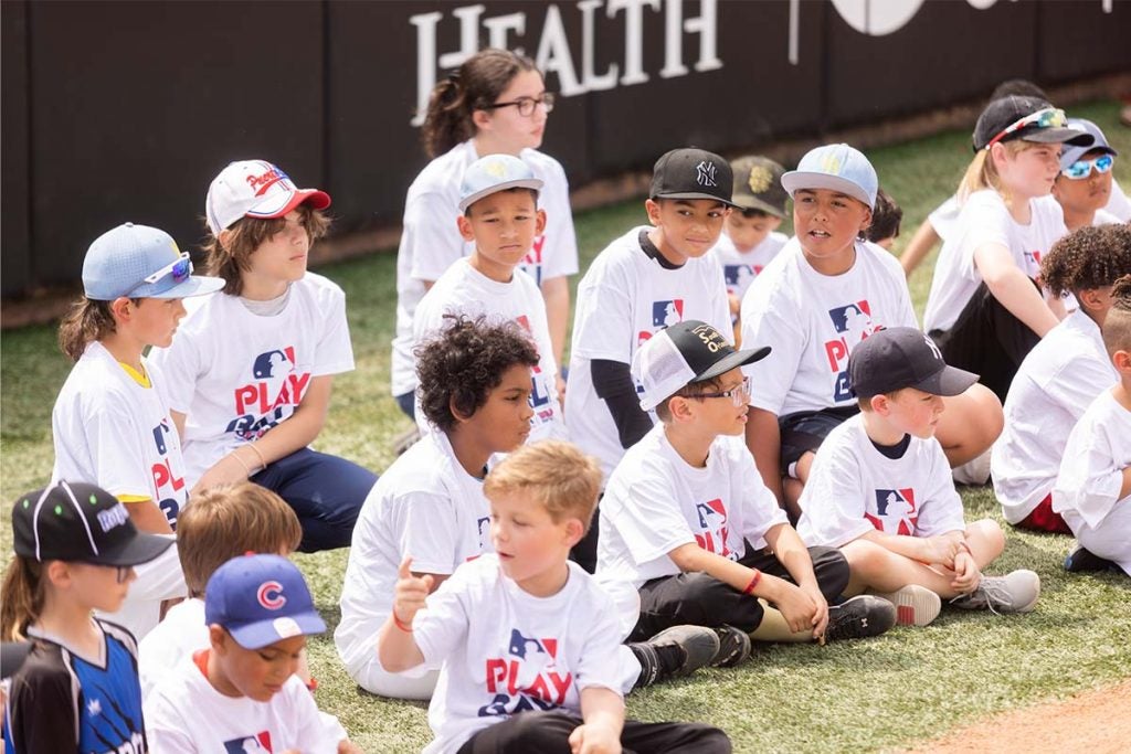 A group of kids sit on a softball field