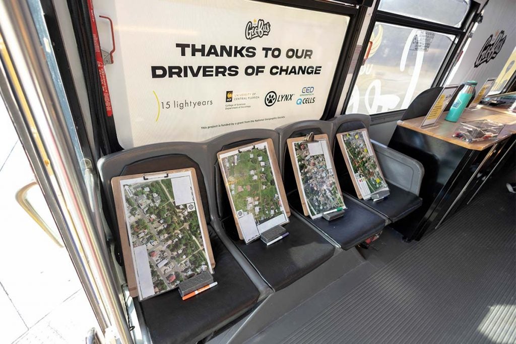 A diagonal view of laminated paper maps on clipboards that are sitting upright on four black seats at the front of the GeoBus.