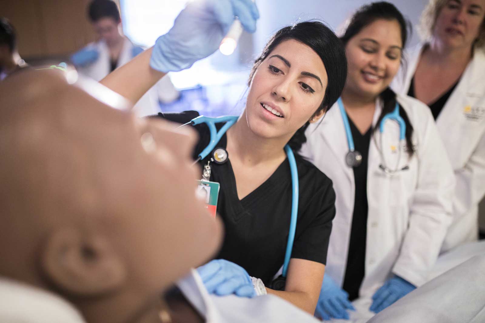 Two nursing students examine a medical manikin as an instructor looks on.