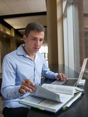 male ucf student studying with laptop and book open