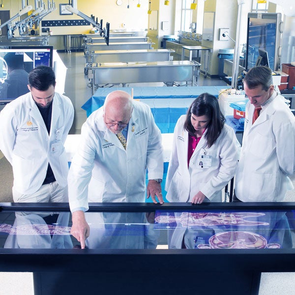 from left to right: two males, one femal, one male, all wearing white lab coats in medical laboratory