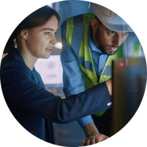 Two professionals reviewing information on a monitor in an industrial setting.