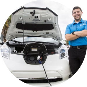 Man standing beside an electric car with its hood open and charging port connected.