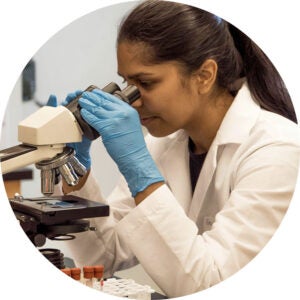 Researcher in gloves examining a sample under a microscope.