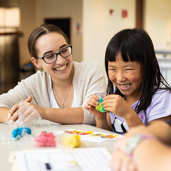 female ucf student sitting at table and looking at little girl smiling and sitting next to her