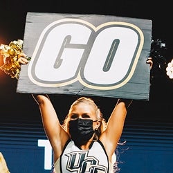 UCF cheerleader wearing face covering holding up a cheer sign