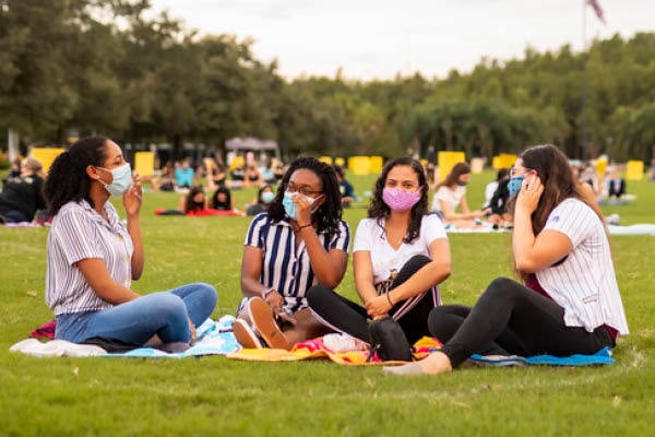 Female students wearing masks and sitting on blankets during The Knighting