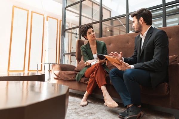 two individuals seated on a couch talking about business