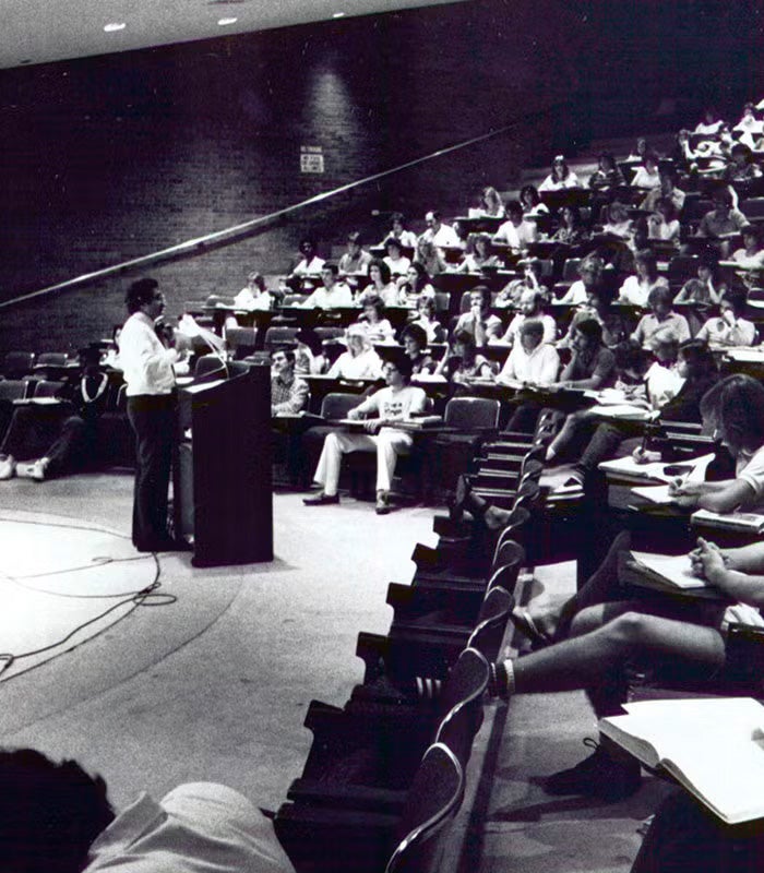 A professor stands at a podium lecturing to students seated in a large, tiered UCF university classroom.