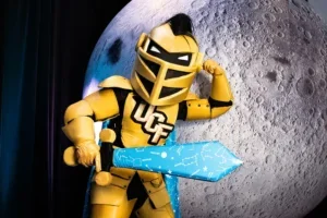 Knightro with constellations on his sword posed in front of a large image of the moon.