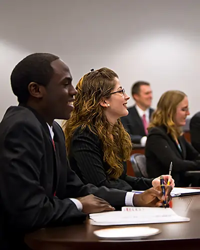 UCF economics students in business attire take notes and engage during a seminar in a classroom.