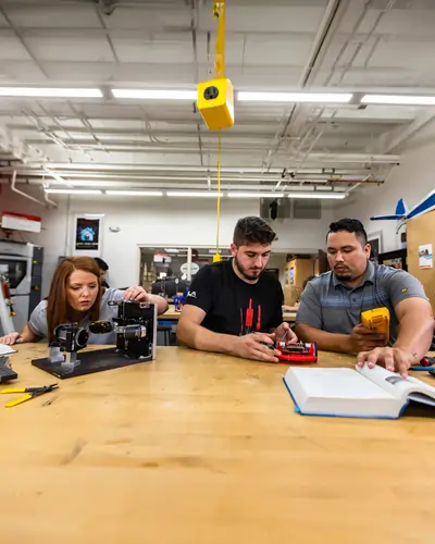 UCF engineering students test small devices with a multimeter at a workshop table inside a campus makerspace.