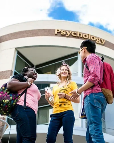 UCF Psychology building with three students engaged in a spirited conversation.