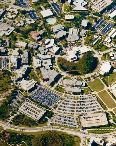 Aerial view of the University of Central Florida campus with ring roads, parking lots, green spaces, and clustered academic buildings.
