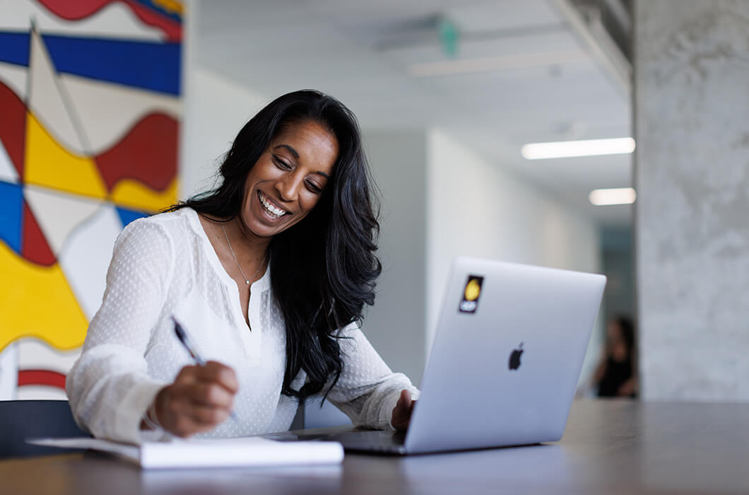 A UCF Online student sits at a desk with her laptop while taking notes on a pad of paper.