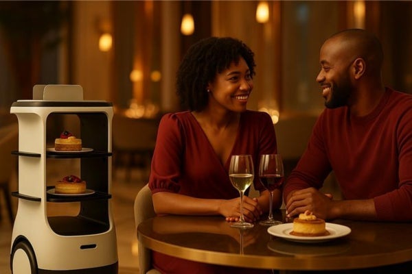A smiling couple in a restaurant with a robotic cart delivering desserts.