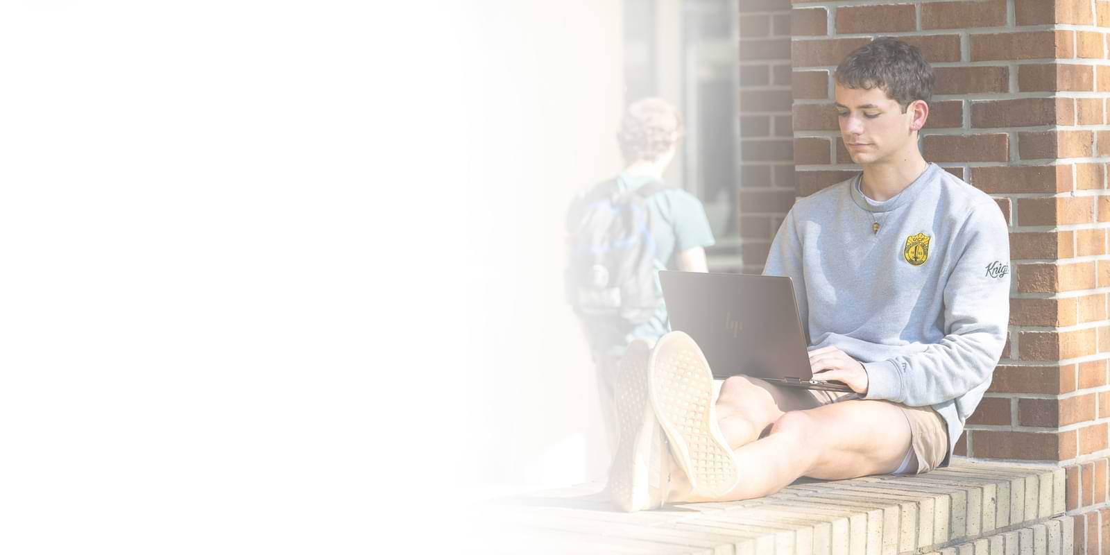 Student outdoors looking contemplatively at their laptop