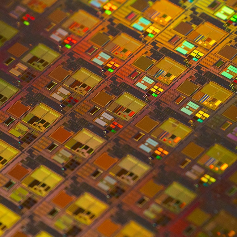 Close-up of a colorful semiconductor wafer with repeating microchip patterns.