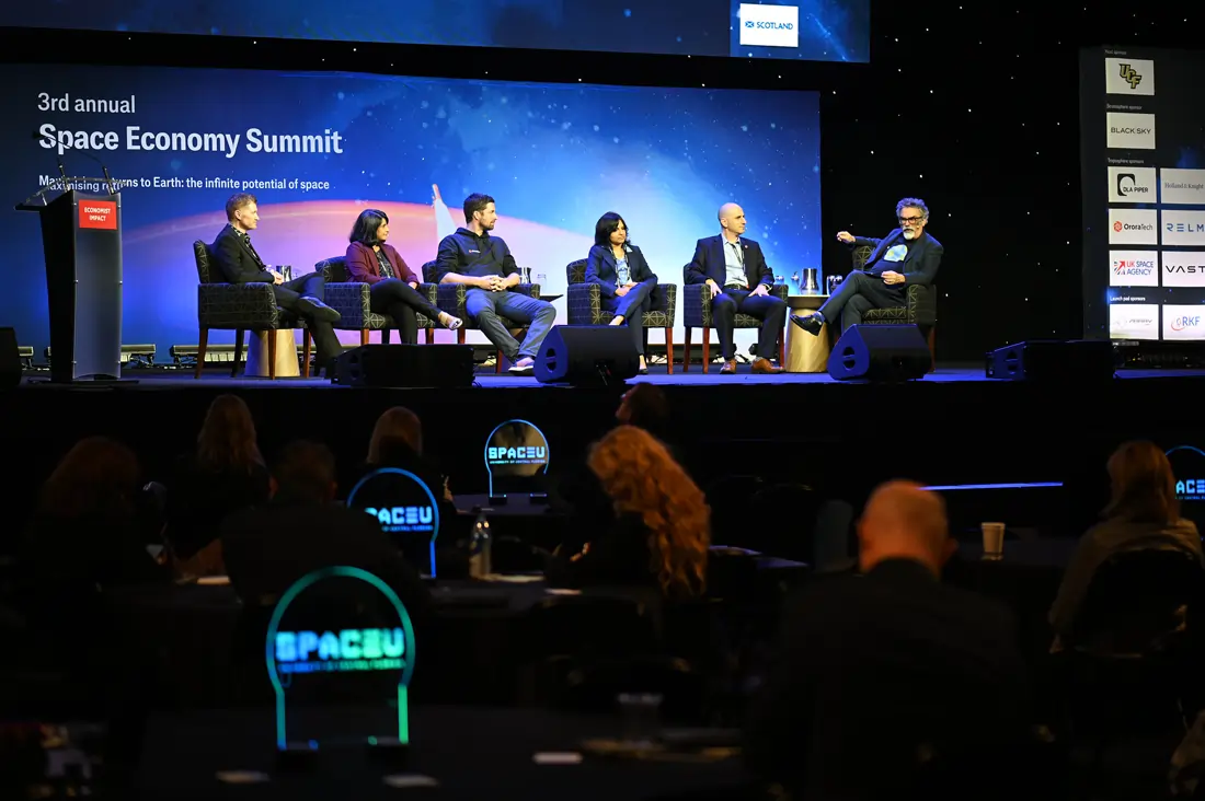 Panelists seated on stage in conversation in front of a screen reading "Space Economy Summit," with an audience seated in the foreground.