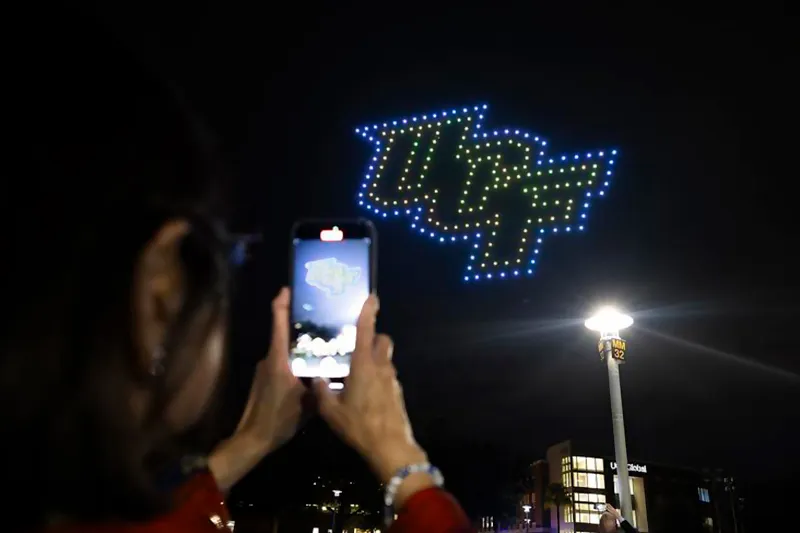 An onlooker snaps an image of group drones in a UCF logo formation during the 2025 Space Week drone show.