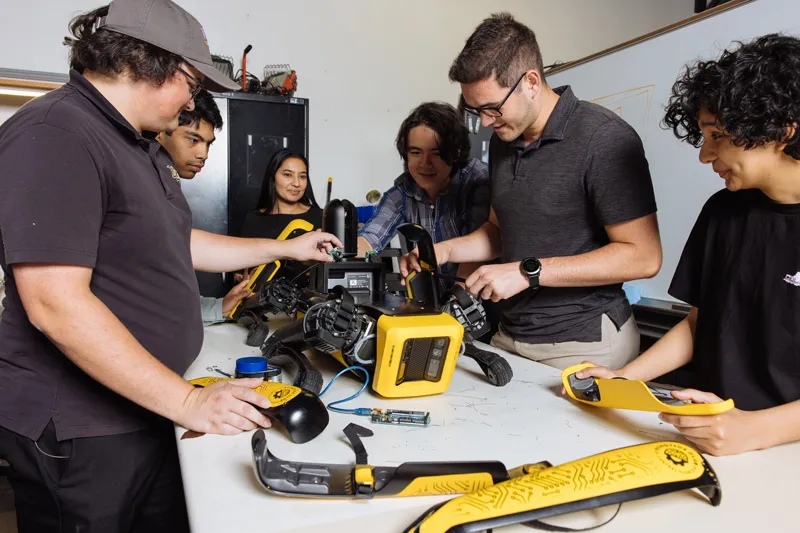 Student collaborate together while assembling a robotic dog on a workbench.