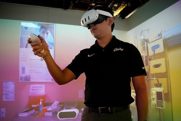 Hiroshi Furuya wearing a virtual reality headset holds a controller while standing in a room to simulate a moon mission.