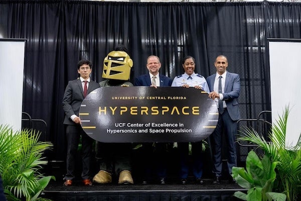 Adam Kotler, Knightro, Alexander N. Cartwright, Col. Janelle T.H. Jackson, and Kareem Ahmed holding a sign for the University of Central Florida Center of Excellence in Hypersonics and Space Propulsion.