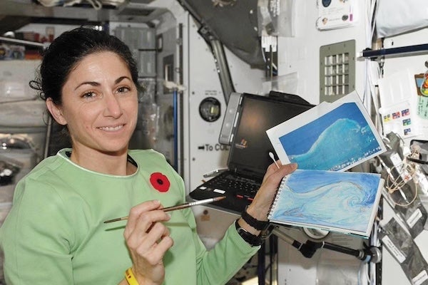 UCF alum Nicole Stott aboard Space Shuttle Discovery holding up The Wave, the first painting completed in space, painted by Stott in 2009.