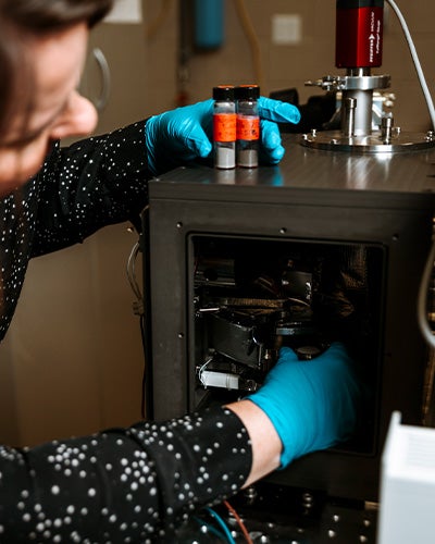 Kerri Donaldson Hanna, wearing blue gloves, places a sample into a laboratory instrument