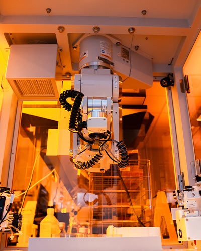 A robotic arm inside an enclosed, orange-lit lab system at UCF’s Biionix Cluster