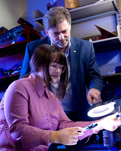Philip Metzger looks on as a student examines a small object under a magnifying lamp
