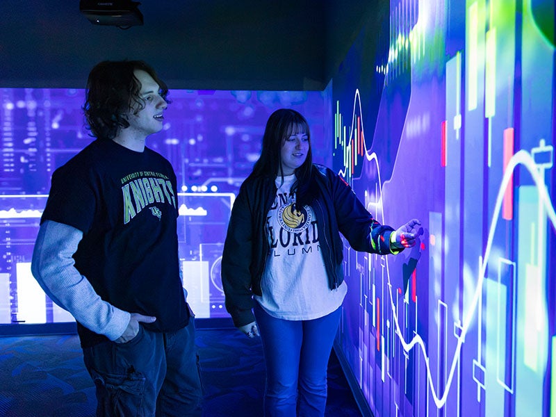 Two students interact with financial charts on an immersive display.