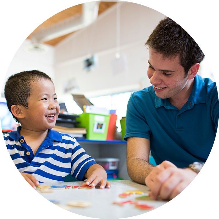 Teacher and young student smile while working together at a classroom table.