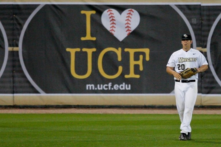 UCF Baseball player standing in front of banner "I (heart) UCF"