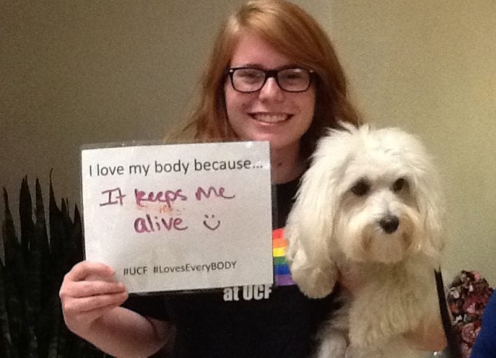 ucf student holding puppy and sign that says "i love my body because it keeps me alive'