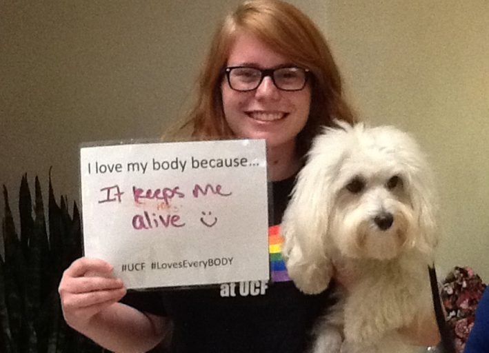 ucf student holding puppy and sign that says "i love my body because it keeps me alive'