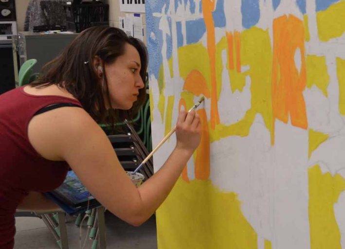 Art student Catie Bopp paints a backdrop for “A Sunday Afternoon on the Island of La Grande Jatte” by Seurat. She also will be a 3-D character in the display.