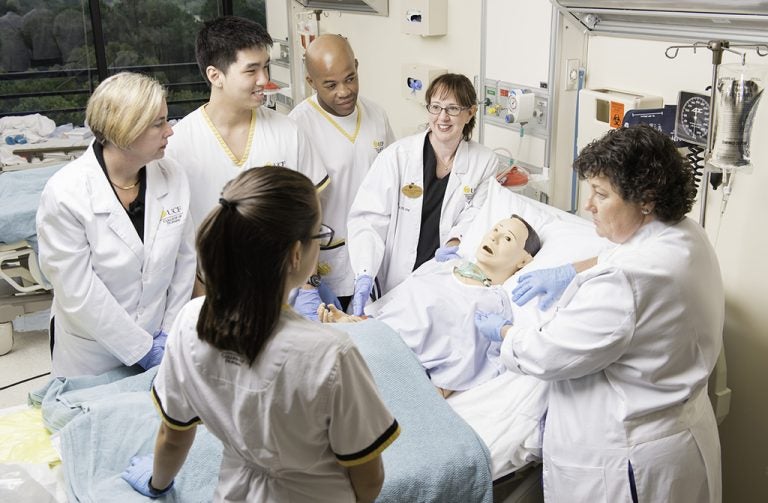 group of ucf college of nursing students standing around patient bed in white lab coats