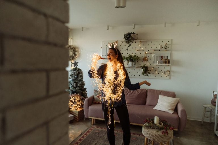 woman with lights draped around her sings in living room