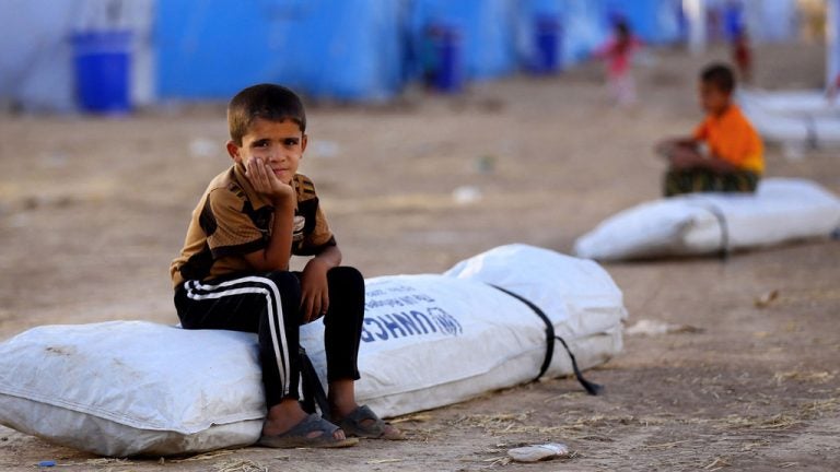 refugee child sitting on used body bag