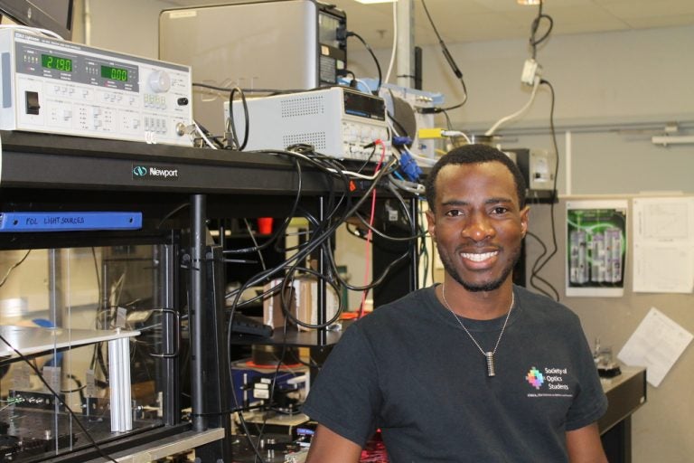 Optics & Photonics and Engineering student Burdley Colas poses next to the equipment in CREOL's Fiber Optics Lab.