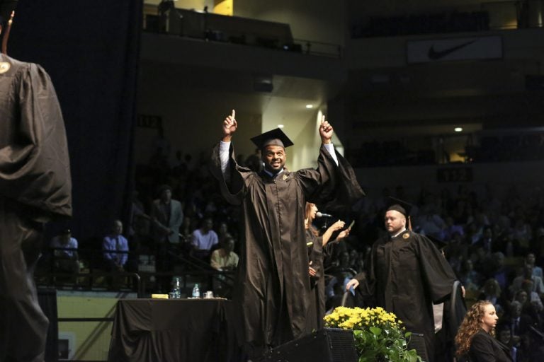 male walking at graduation with arms in air holding diploma