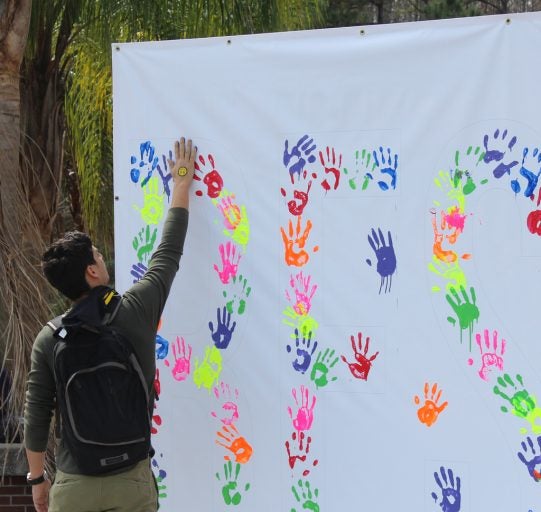student puts paint handprint on white sheet along with others