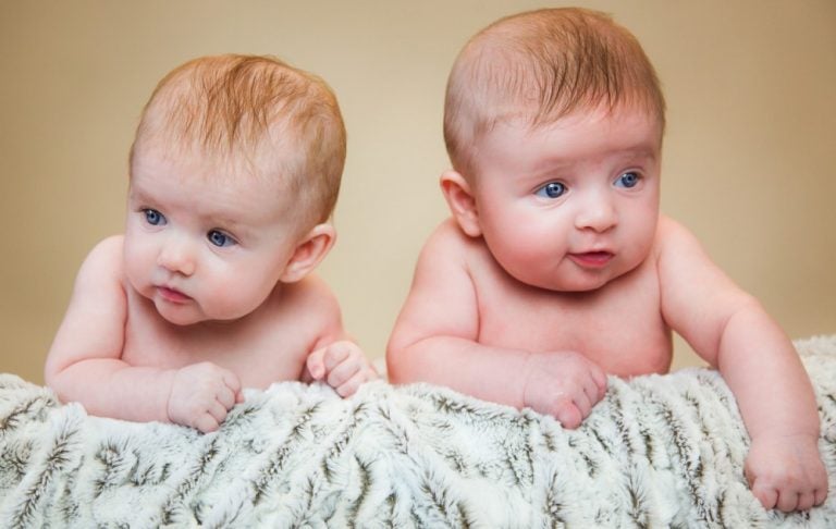 two babies sitting against a prop with blanket