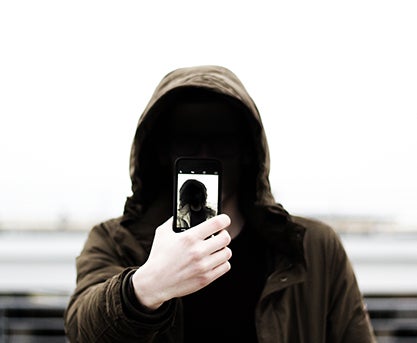 person in hoodie holding up cell phone with right hand, taking a selfie