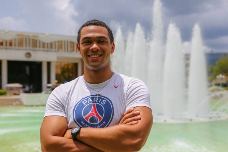 muscular male ucf student standing in front of ucf reflecting pond facing camera, smiling, with arms crossed